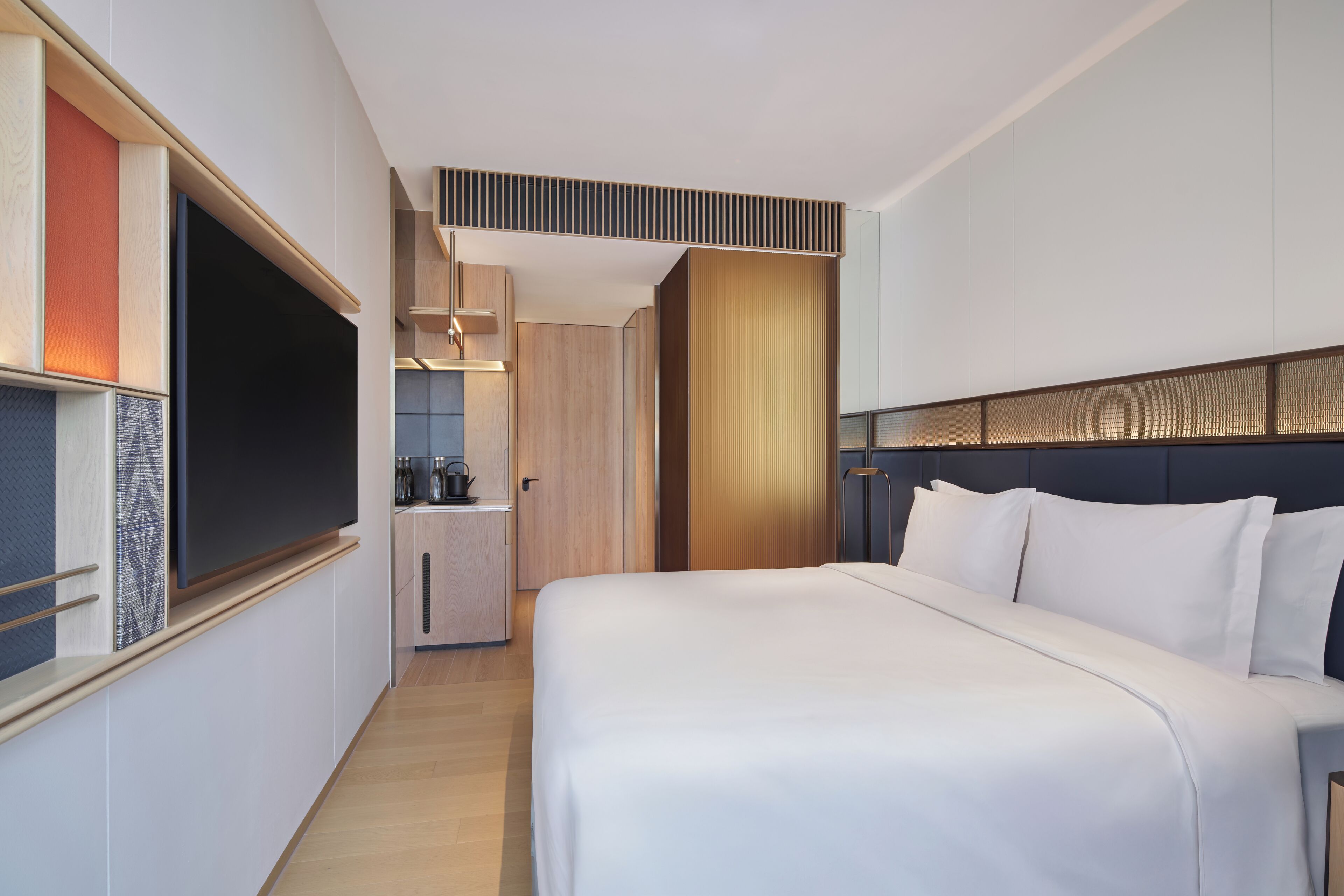 Een moderne hotelkamer met een groot bed, een televisie, een kitchenette en een inloopkast.