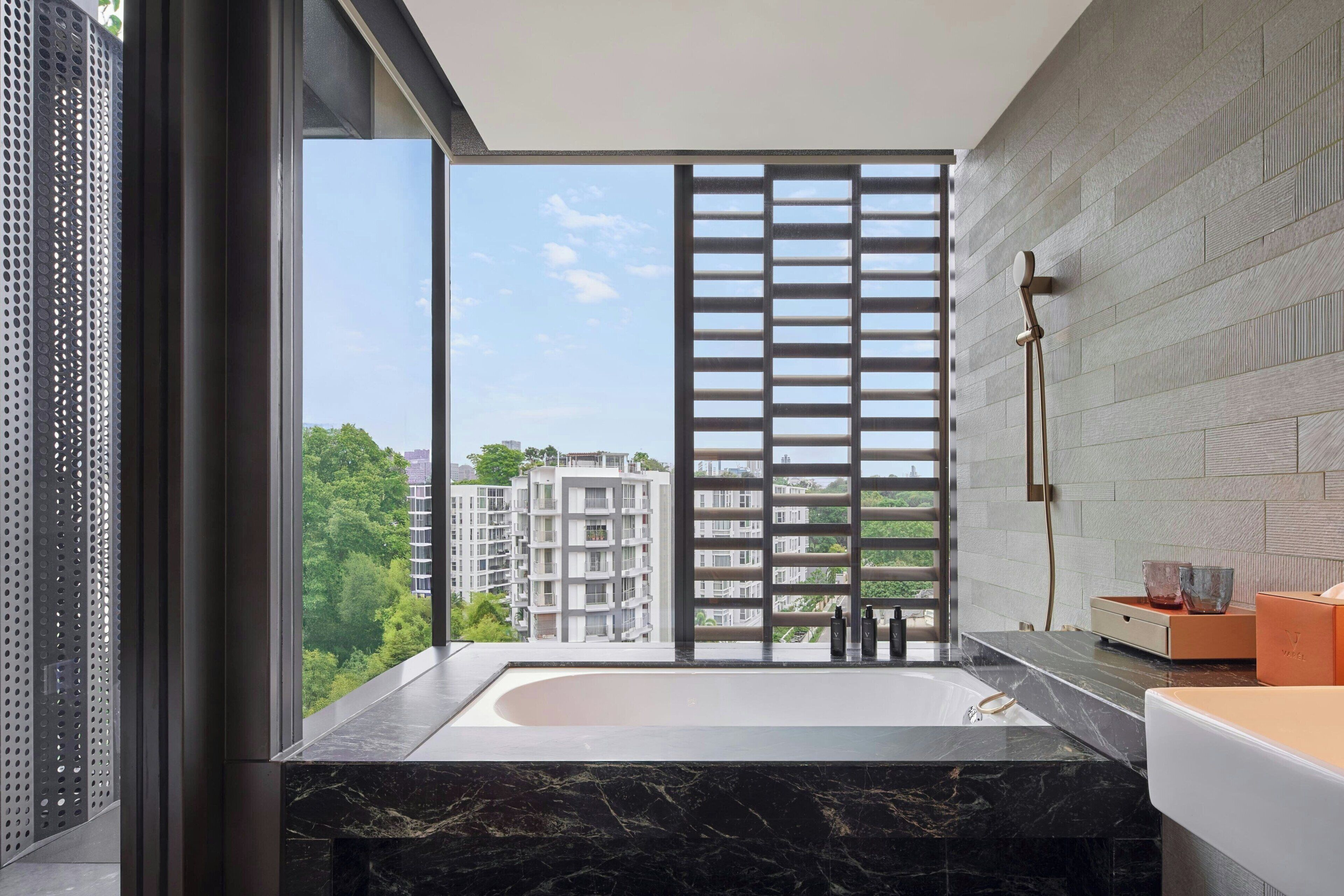 A modern bathroom with a large bathtub, a glass shower enclosure, and a view of buildings through a window.