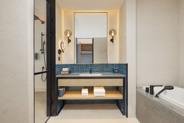 A modern bathroom with a glass shower enclosure, a sink with a blue tiled backsplash, and a bathtub.