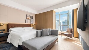 Una habitación de hotel moderna con una cama grande, un sofá, un televisor y vistas a la ciudad.