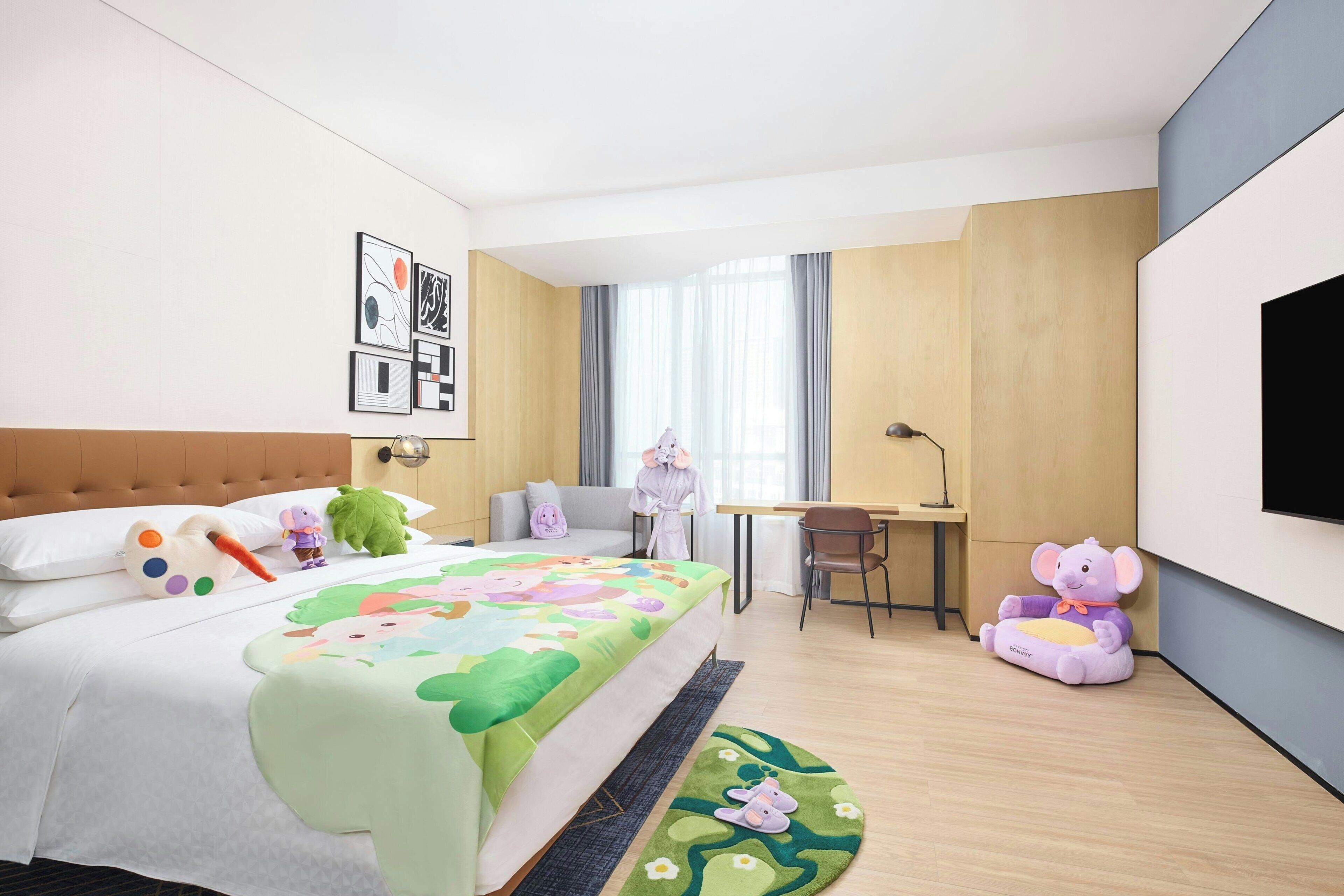 Ein Hotelzimmer mit Bett, Schreibtisch, Stuhl, Fernseher und einem Kuscheltier.