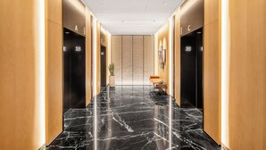 Un pasillo moderno con pisos de mármol negro, paneles de madera y dos ascensores indicados con los números 18.