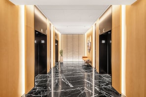 Un pasillo moderno con pisos de mármol negro, paneles de madera y dos ascensores indicados con los números 18.