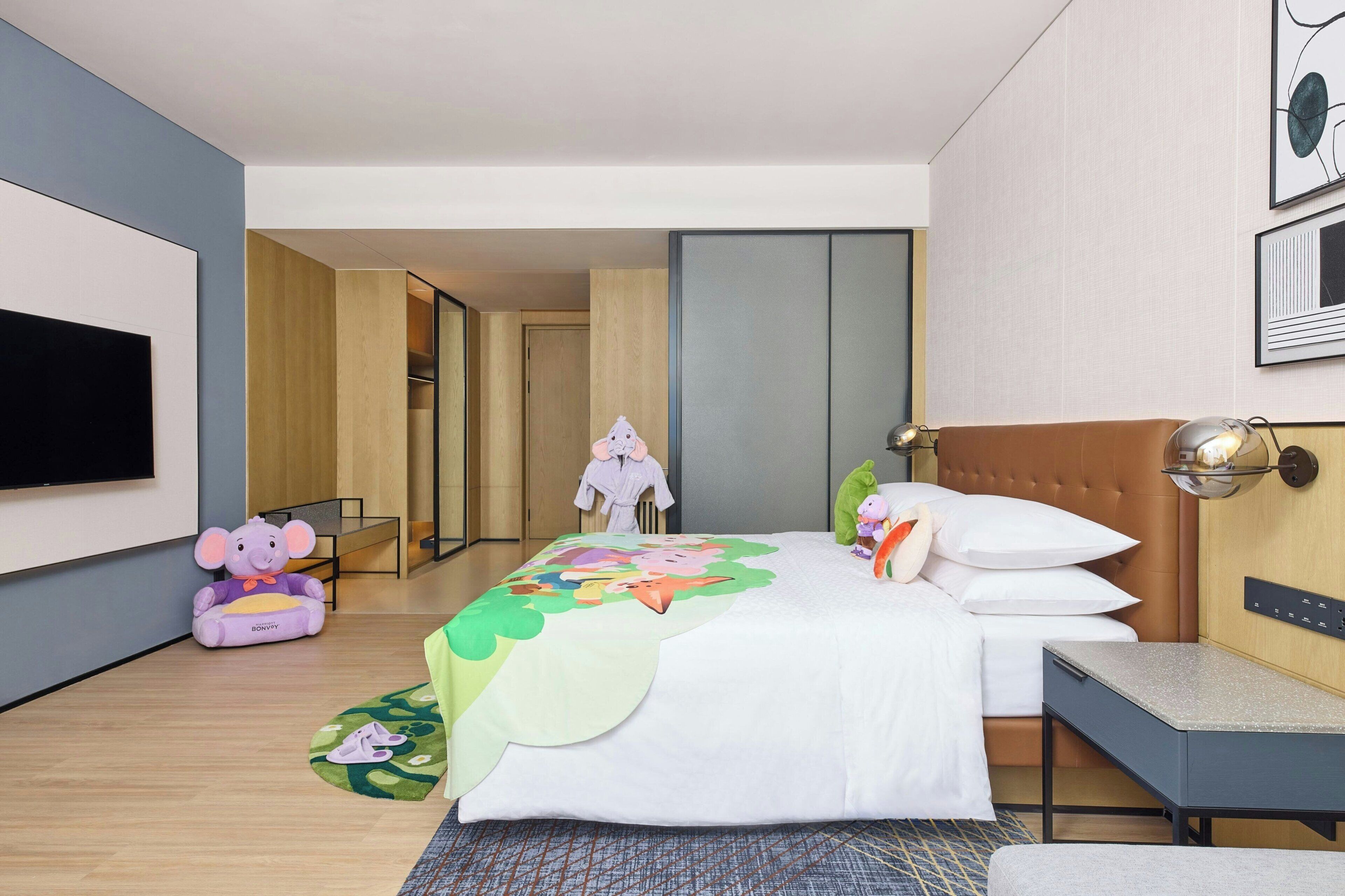Habitación de hotel con cama, escritorio, televisor y lámpara en la pared.