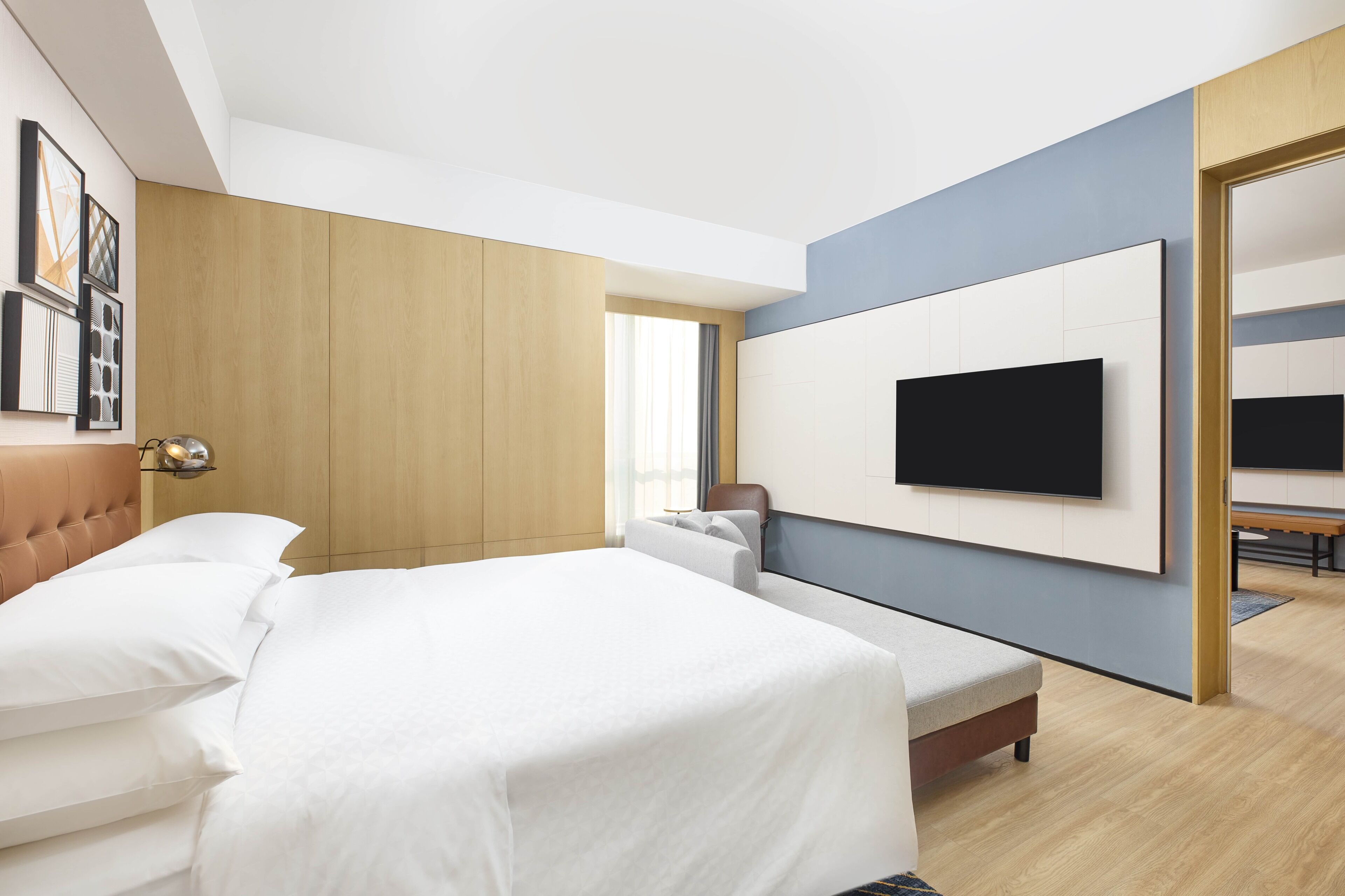 Une chambre d’hôtel moderne dotée d’un grand lit, d’un téléviseur à écran plat fixé au mur et d’une armoire en bois.