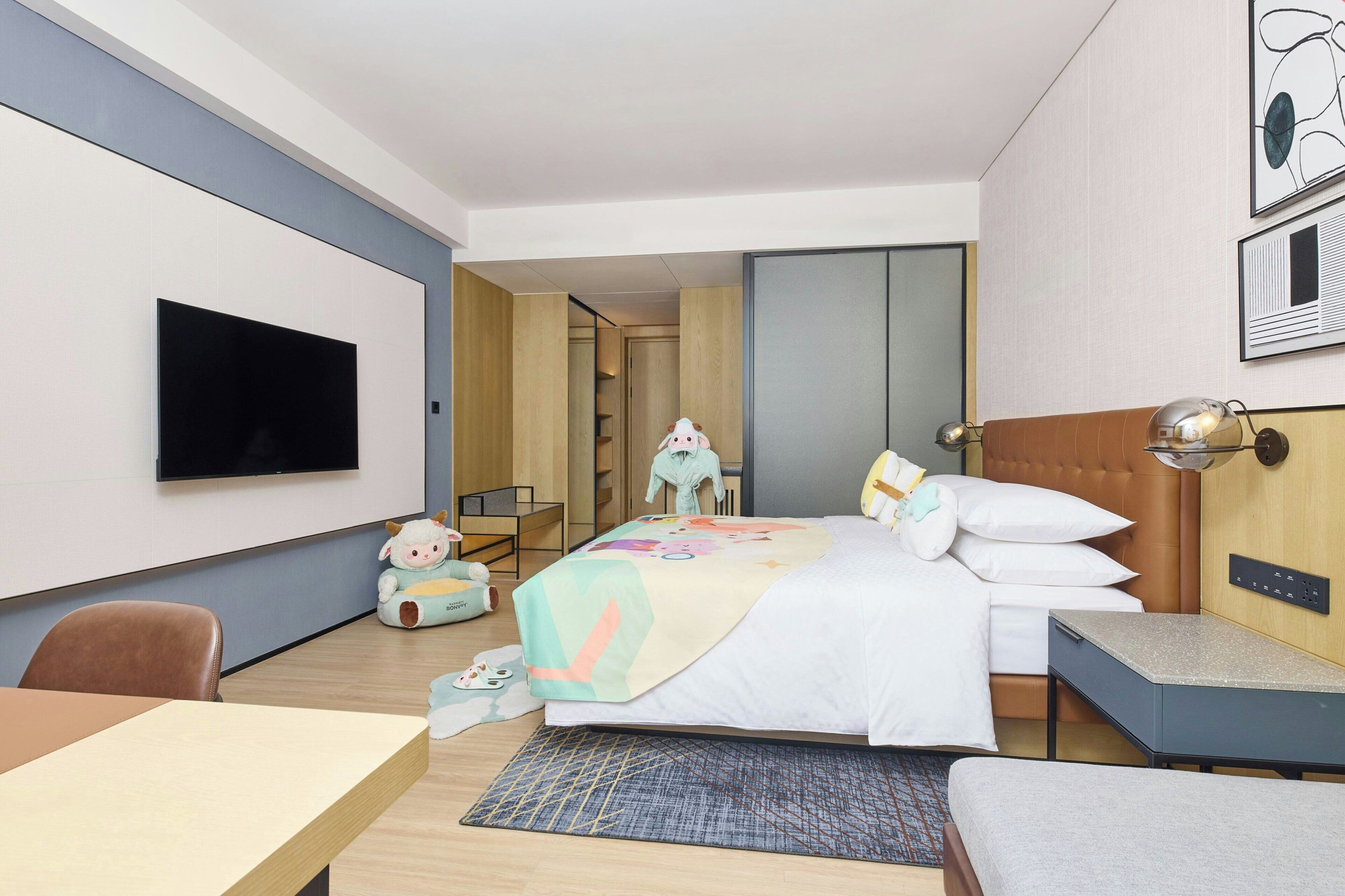 Una habitación de hotel con cama, mesita de noche, silla, televisor y una pequeña mesa con otra silla.