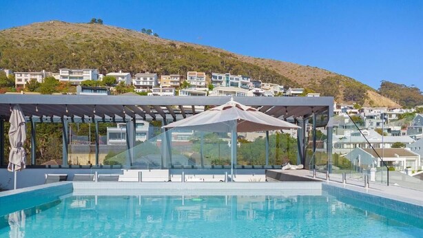 Une piscine dotée d’une pergola et de chaises longues, située dans un quartier résidentiel en pente.