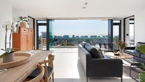 Un salon moderne avec un canapé, une table à manger et des chaises. De grandes fenêtres offrent une vue sur la ville.