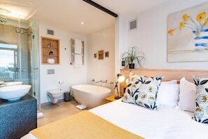 A modern bathroom with a freestanding bathtub, a glass-enclosed shower, and a vanity with a large sink. - The Murex (Cape Town)