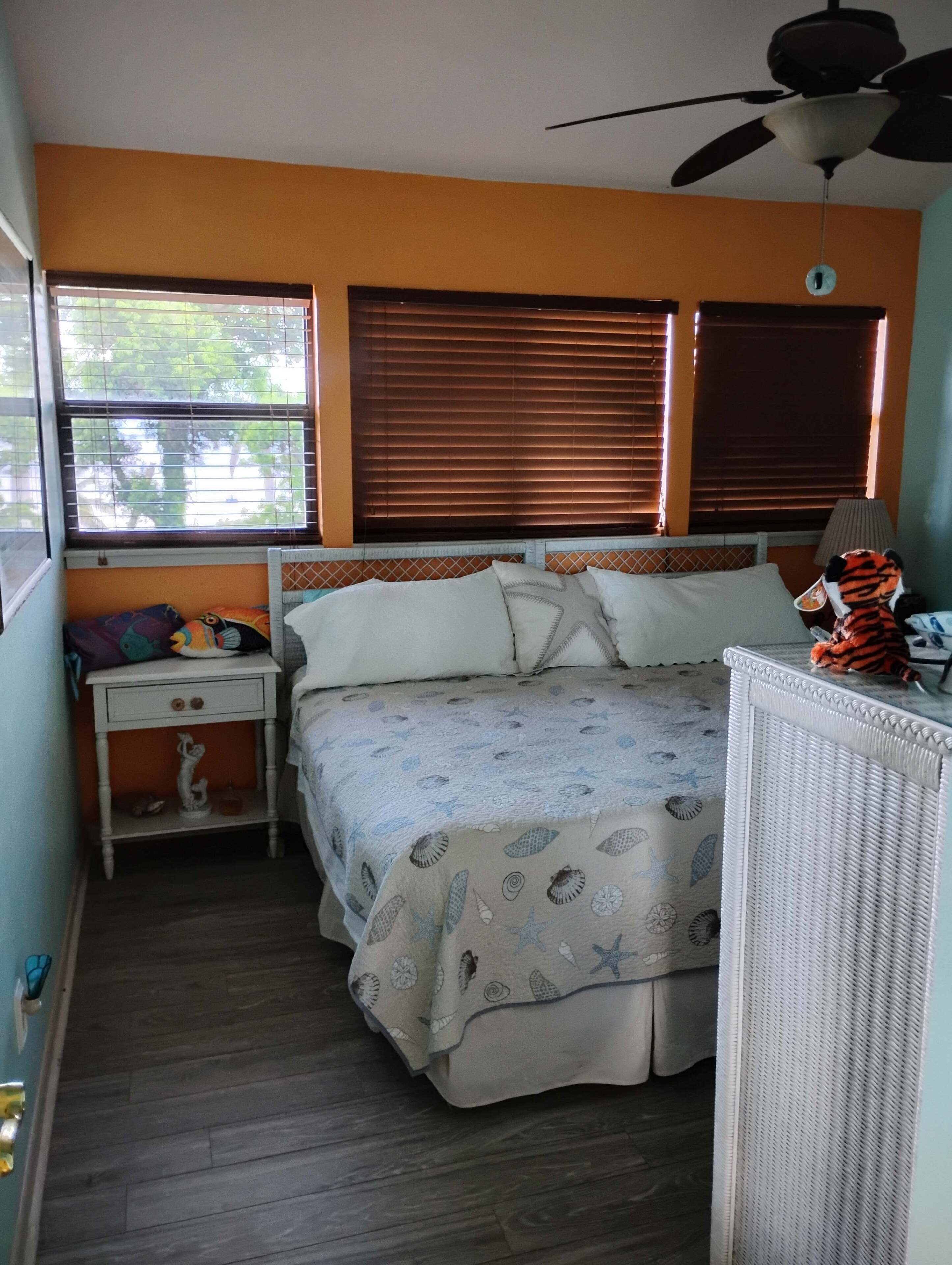 A bedroom with a bed, a nightstand, a dresser, a ceiling fan, and windows with blinds.