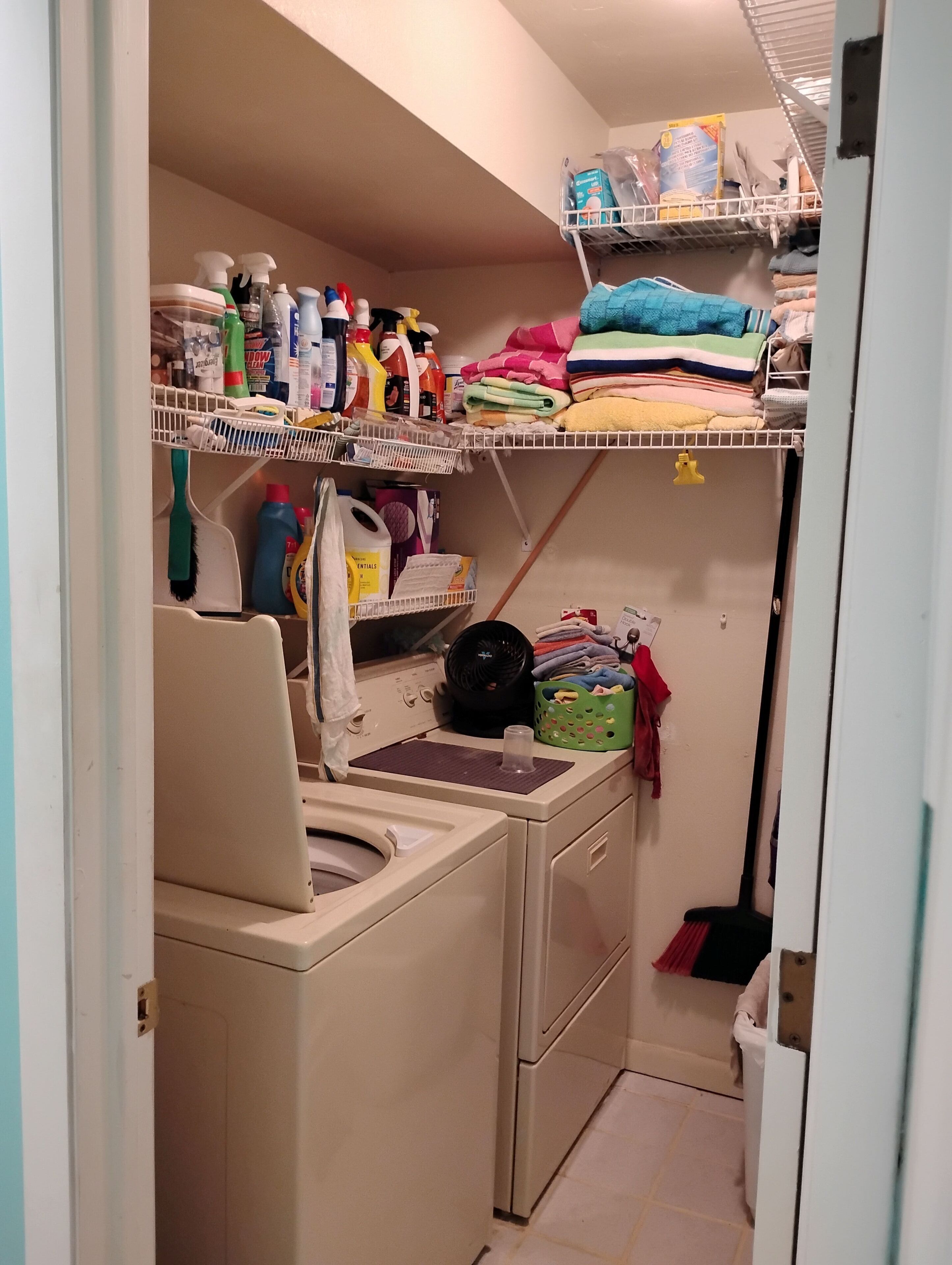 Un área de lavandería con lavadora, estantes con productos de limpieza y ropa doblada.