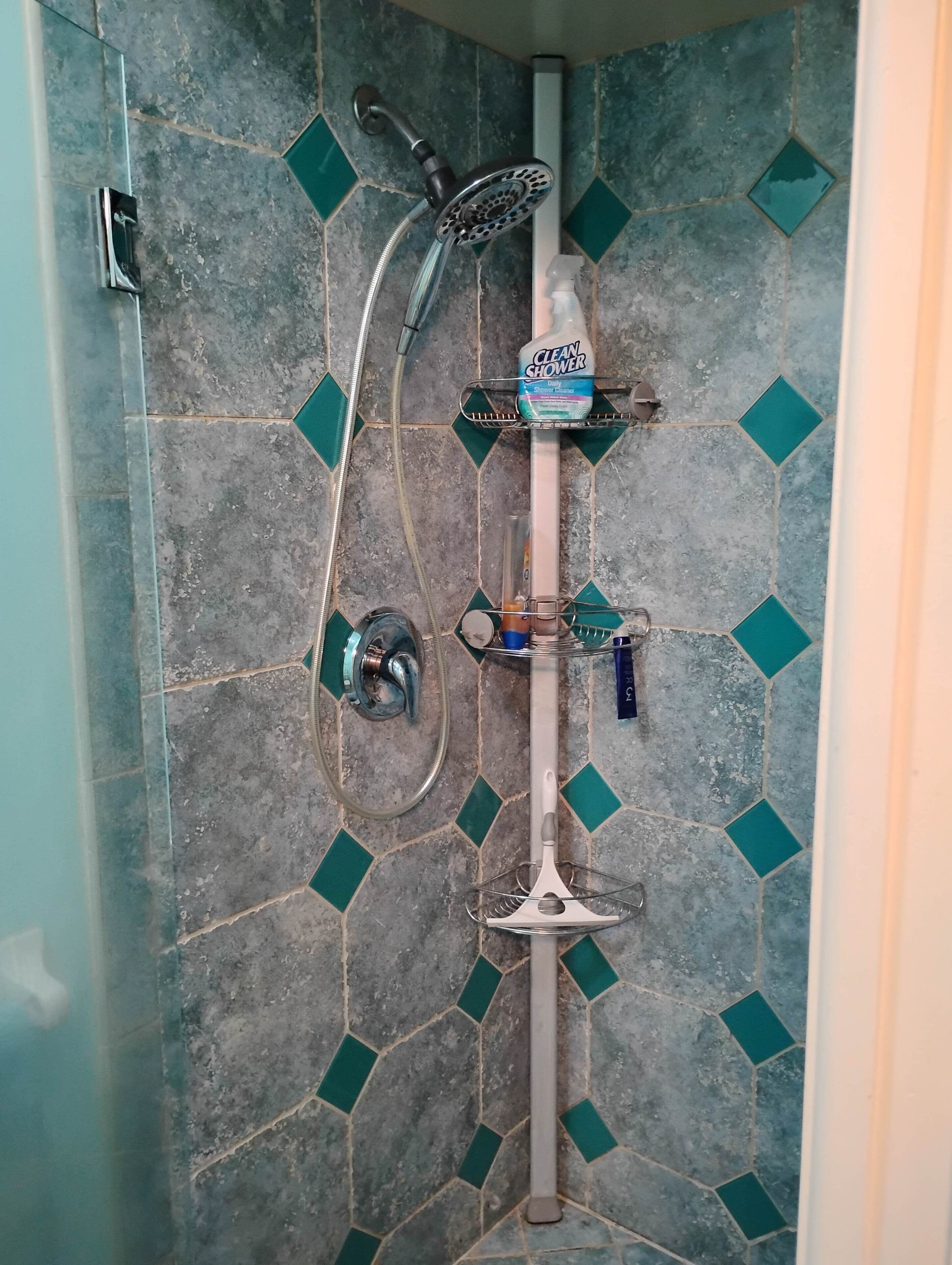 Una ducha con cabezal de ducha de mano, grifo empotrado en la pared y una botella de limpiador para ducha.
