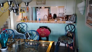 Un coin repas avec une table et des chaises en verre, une cuisine à l’arrière-plan et un panneau décoratif sur le mur.