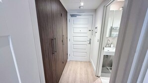 A narrow hallway with a wooden wardrobe, a white door, and a bathroom visible through an open door.
