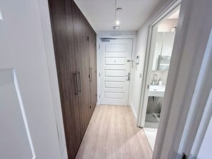 A narrow hallway with a wooden wardrobe, a white door, and a bathroom visible through an open door. - Fully Furnished Studio Apt with AC & Lift in St John's Wood near Regent's Park (London)