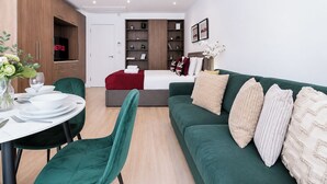 A modern living room with a green sofa, a dining table with chairs, a TV, and a bookshelf.