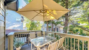 Une terrasse extérieure couverte, dotée d’une table et de chaises, entourée d’une rambarde en bois et agrémentée de plantes en pot.
