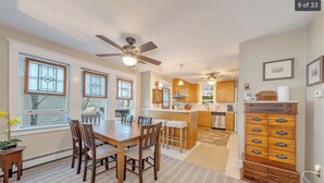 Une cuisine moderne avec des meubles en bois, un coin repas doté d’une grande table et de chaises, et un ventilateur de plafond.