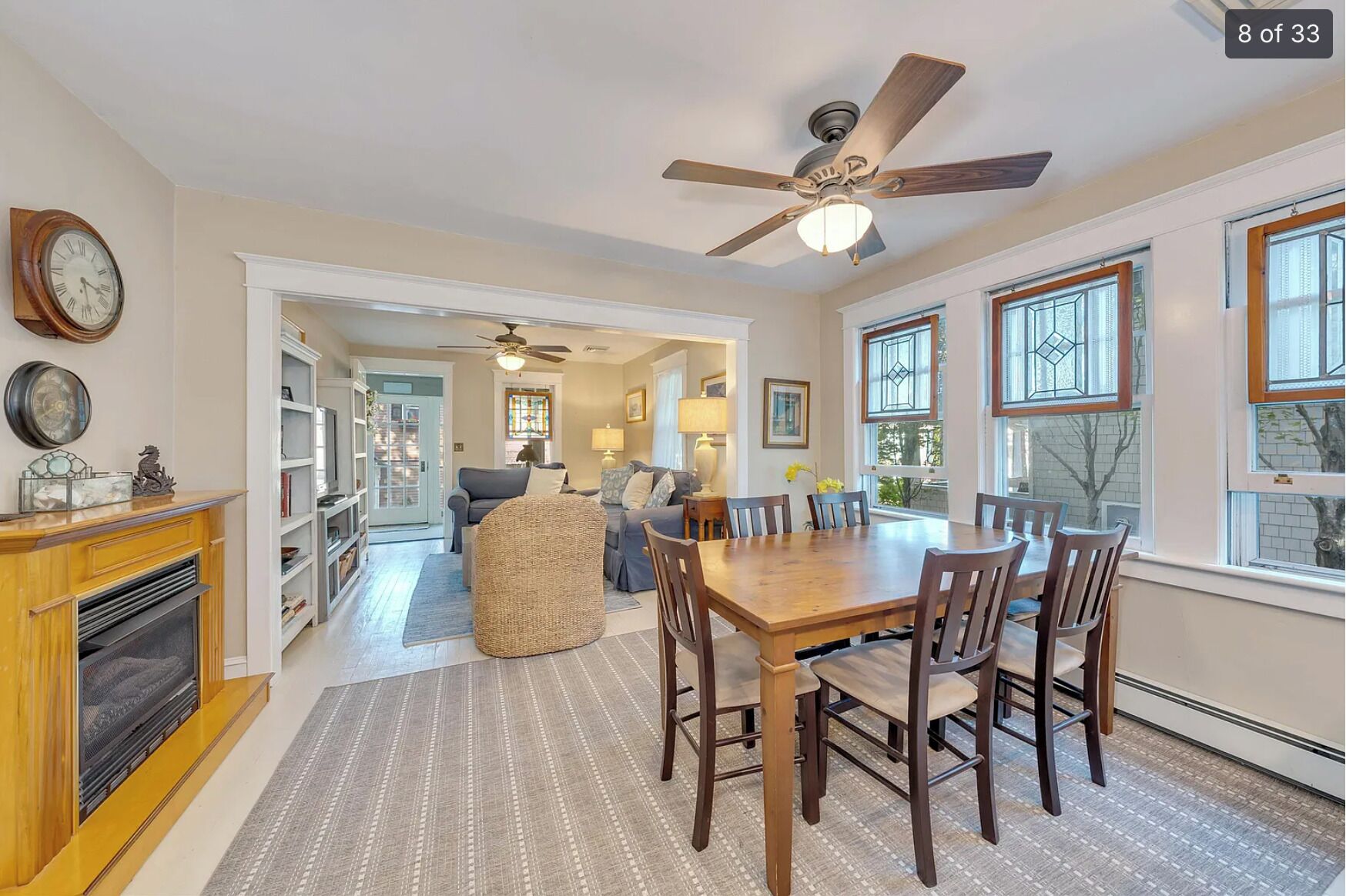 A spacious living room with a fireplace, a dining area with a wooden table and chairs, and a ceiling fan.