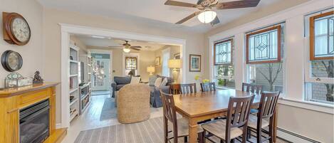 A spacious living room with a fireplace, a dining area with a wooden table and chairs, and a ceiling fan.