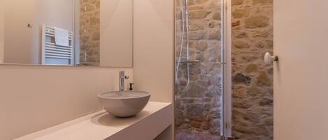 Un baño moderno con pared de piedra, lavamanos blanco y ducha con cerramiento de vidrio.