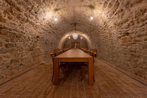 A stone-walled room with a long wooden table and chairs, a chandelier, and a tiled floor. - Palazzo Serre - Villa in the Countryside With Pool (San Leo)
