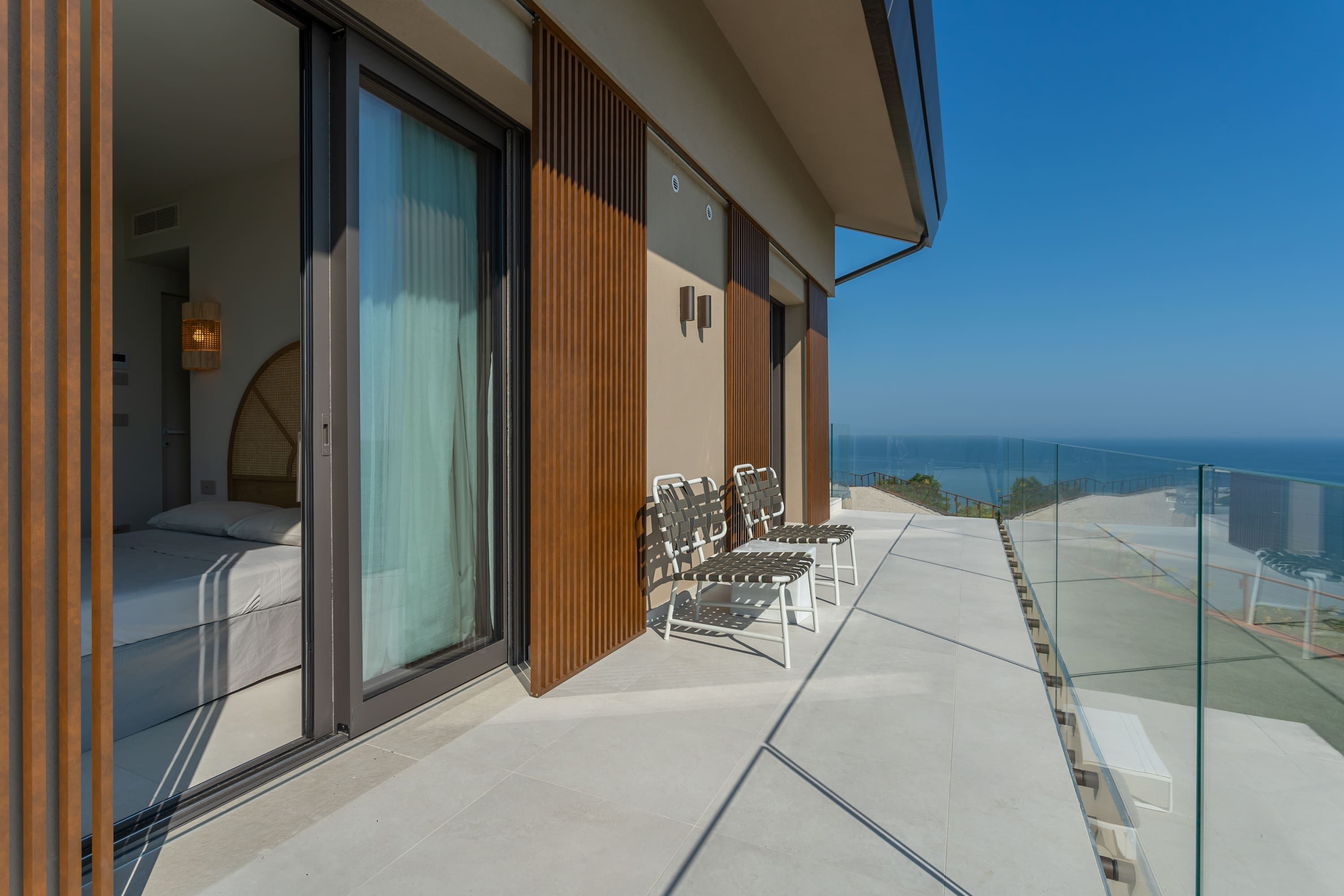 A balcony with a bed, a seating area, and a view of the ocean.