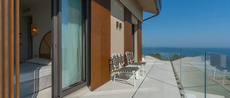 A balcony with a bed, a seating area, and a view of the ocean.
