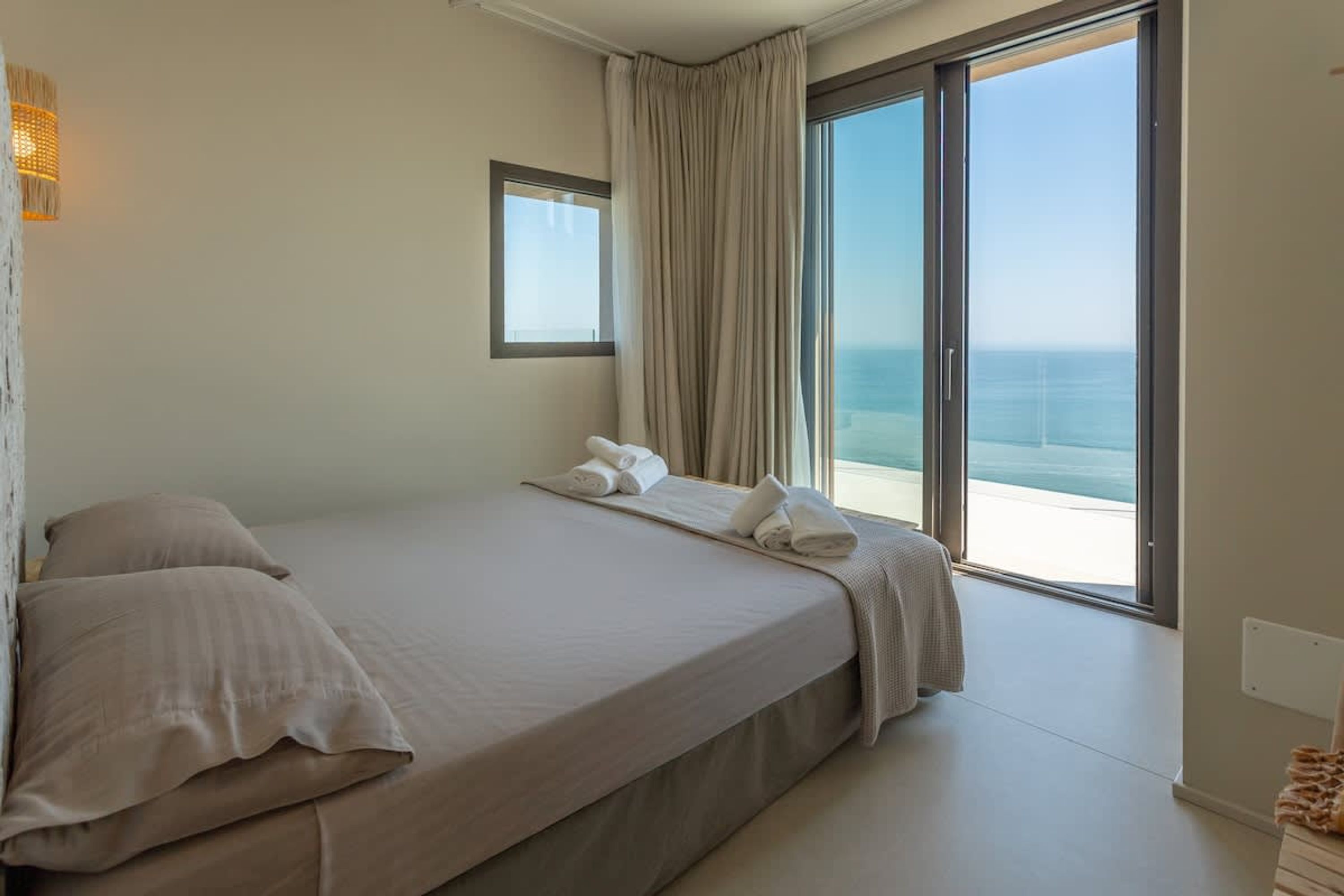 A bedroom with a large bed, a window, and a view of the sea.