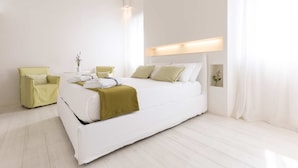 Een moderne slaapkamer met een groot bed, een groene fauteuil en een nachtkastje met een bloevas.