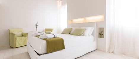 A modern bedroom with a large bed, a green armchair, and a bedside table with a vase of flowers.