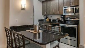 Une cuisine moderne avec des meubles en bois foncé, des appareils électroménagers en acier inoxydable et un coin repas comprenant une table et des chaises.