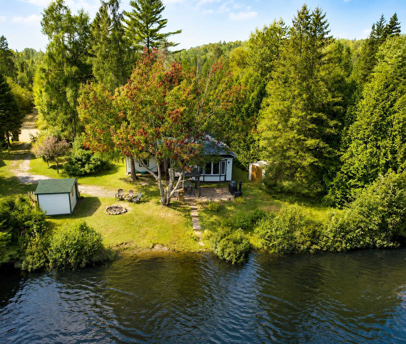 A lakeside cabin with a deck, surrounded by dense forest and a small dock.