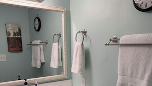 Un baño con tocador blanco, un espejo grande con luces, un reloj y toallas colgadas en ganchos.