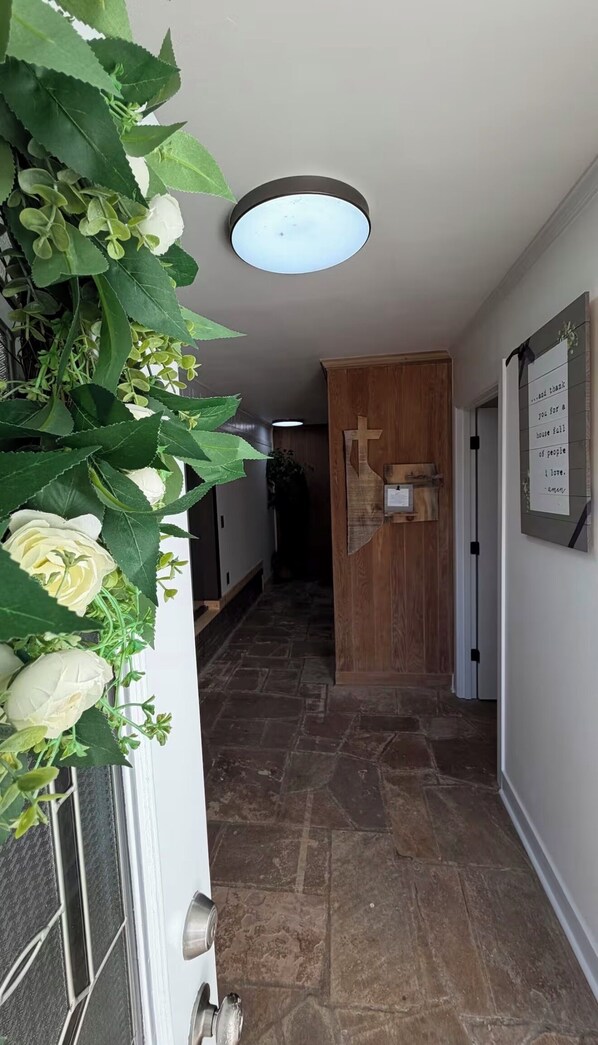 A hallway with stone flooring, a wooden door with a cross, and a wall-mounted sign. - Oak & stone (Dalton)