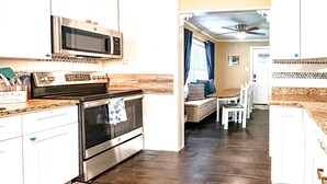 A kitchen with a microwave, oven, and stove. There is a dining area with a table and chairs. - 3Br 2Ba Cottage w/ Golf Cart (Waveland)