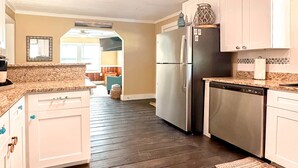 A kitchen with dark wooden flooring, white cabinets, a stainless steel refrigerator, and a dishwasher. - 3Br 2Ba Cottage w/ Golf Cart (Waveland)