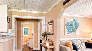 A hallway with wooden flooring, a sofa with cushions, a table with a vase, and a painting on the wall. - 3Br 2Ba Cottage w/ Golf Cart (Waveland)
