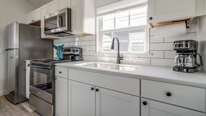 Una cocina moderna con armarios blancos, electrodomésticos de acero inoxidable, un lavamanos doble y un ventanal sobre el fregadero.
