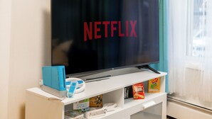 A flat-screen TV on a white entertainment unit with a remote control, a blue game console, and some books. - Quiet & Walkable - Stampede, BMO, Nightlife & Eats - Apartment (Calgary)