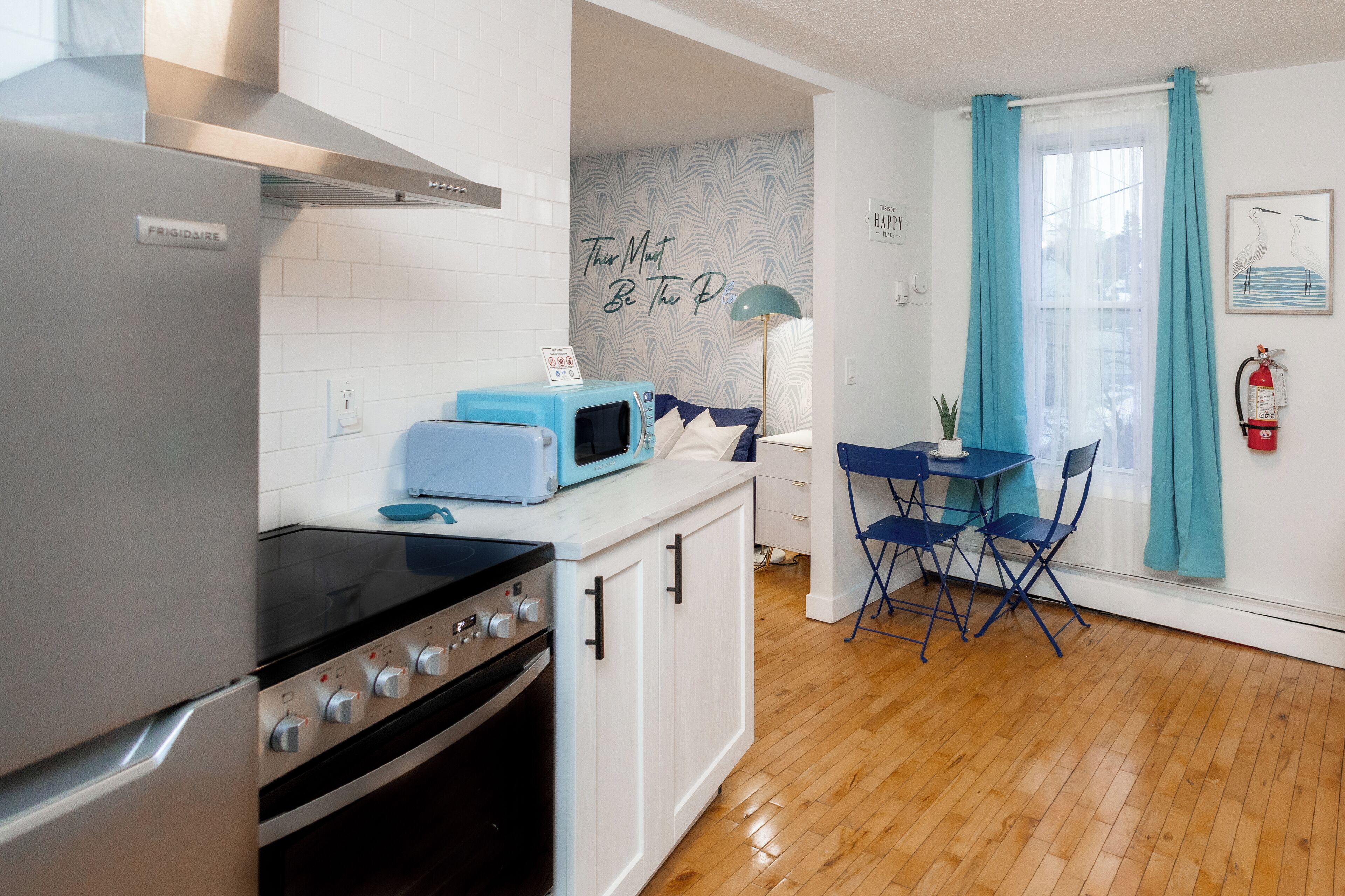 A compact kitchen with a refrigerator, stove, and microwave. There is a dining area with a table and chairs.