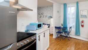 A compact kitchen with a refrigerator, stove, and microwave. There is a dining area with a table and chairs. - Quiet & Walkable - Stampede, BMO, Nightlife & Eats - Apartment (Calgary)
