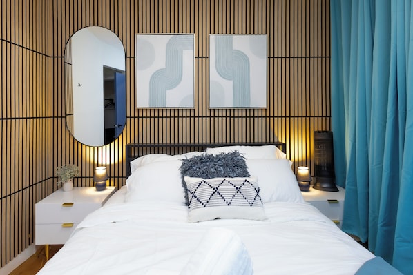 A modern bedroom with a bed, two bedside tables, a mirror, and abstract wall art.