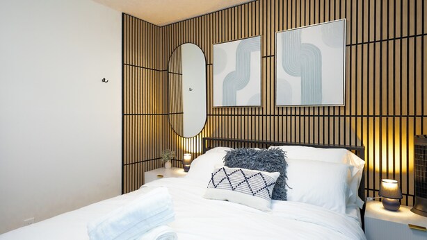 A neatly made bed with white linens and a blue blanket, a bedside table with a lamp, and two wall-mounted artworks. - Quiet & Walkable - Stampede, BMO, Nightlife & Eats - Apartment (Calgary)