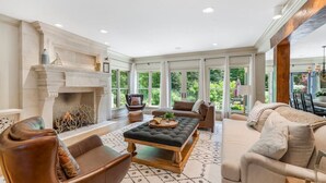 Un salon spacieux doté d’une cheminée, de fauteuils en cuir, d’un canapé et d’une grande fenêtre donnant sur un paysage verdoyant.