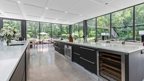 Eine moderne Küche mit großen Fenstern, einer zentralen Kochinsel und einem Essbereich mit Sitzgelegenheiten im Freien.