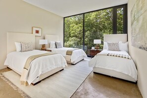 Une chambre moderne avec deux lits, de grandes fenêtres et une vue sur les arbres.