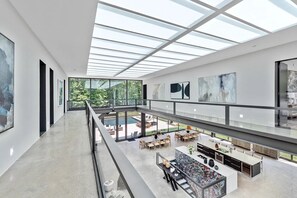 Un intérieur spacieux et moderne, doté d’un plafond haut et de puits de lumière, un coin repas avec des sièges extérieurs, et une cuisine avec un grand îlot central.