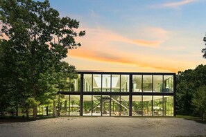 Un bâtiment moderne doté de grandes fenêtres en verre, entouré d’arbres et bordé d’un chemin de gravier.