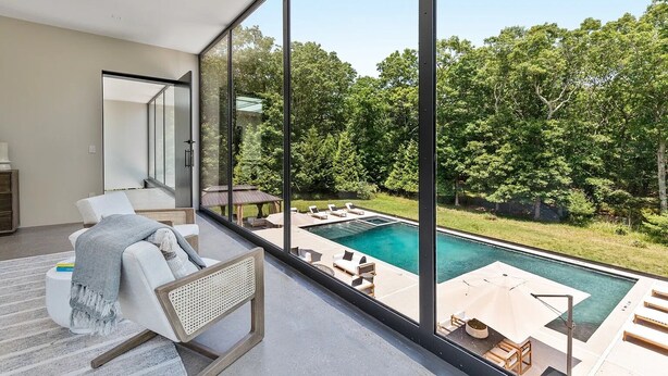 Ein modernes Wohnzimmer mit einer großen Glaswand mit Blick auf einen Swimmingpool und üppiges Grün.
